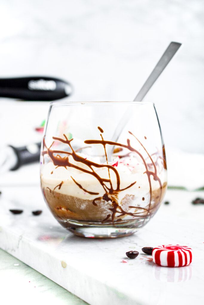 Head on view of a small glass on marble counter with a spoon in it and cholatey creamy liquid in it