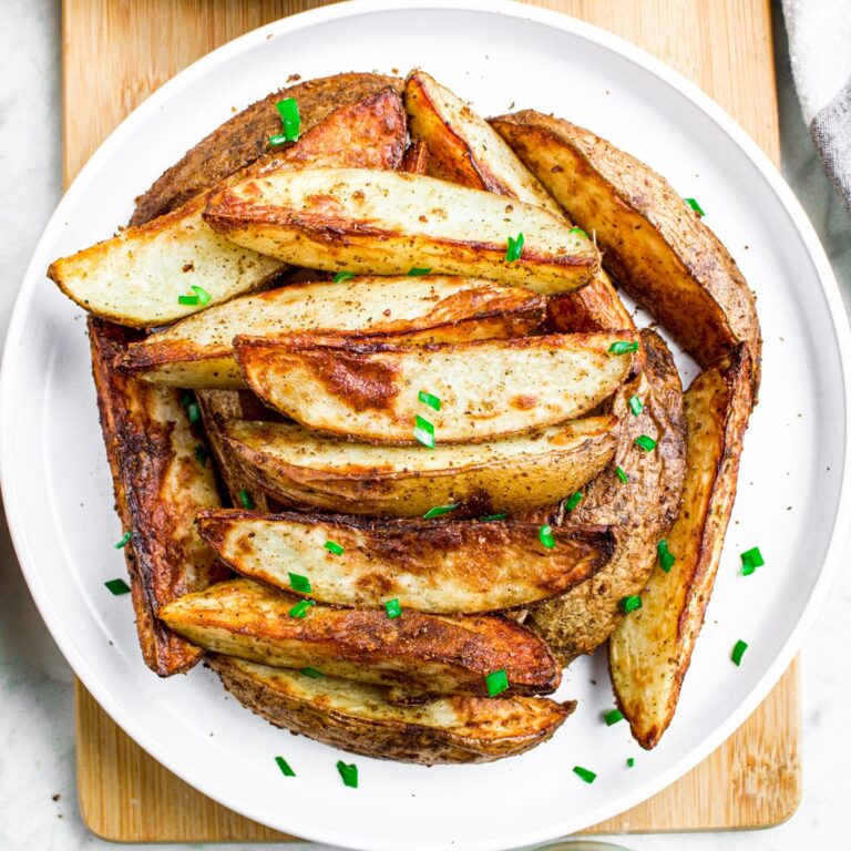 Overhead view of a pile of air fryer potato wedges on a round white plate sprinkled with chives