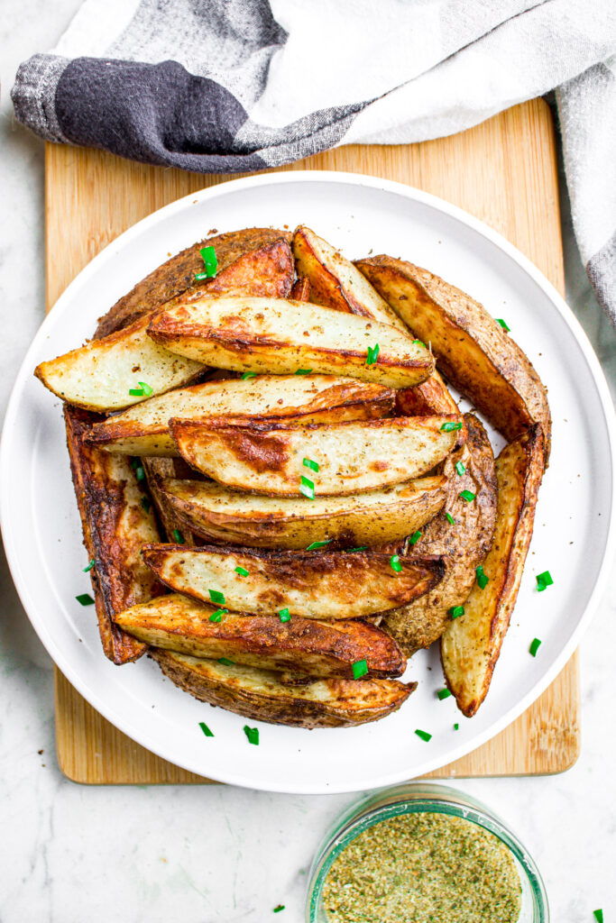 Overhead view of a round white plate of air fryer potato wedges topped with minced green herbs
