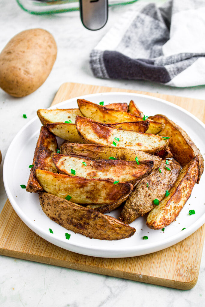 Overhead view of a round white plate piled with wedges on top and a whole potato in the background
