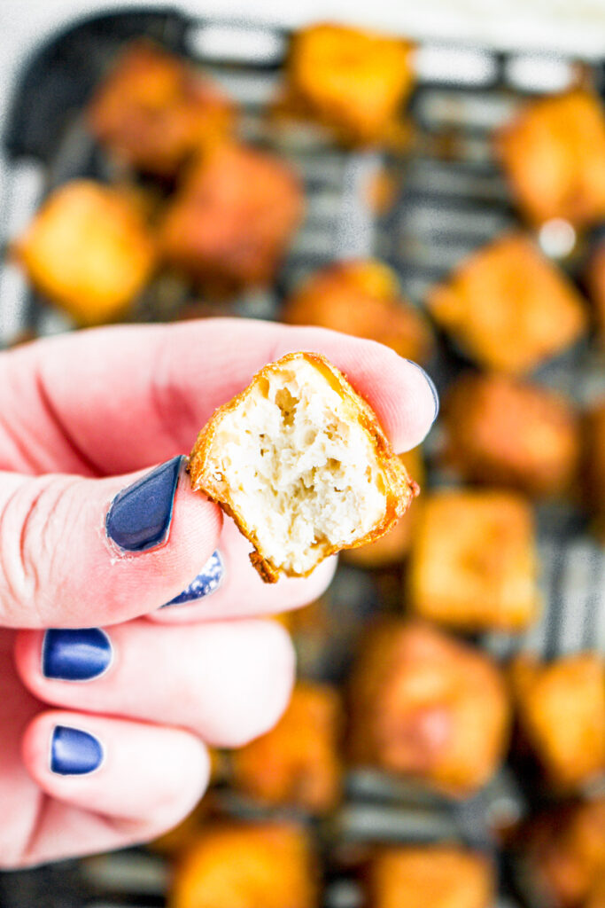 Overhead photo of a hand holding a cooked crispy tofu cube with a bite taken out of it.