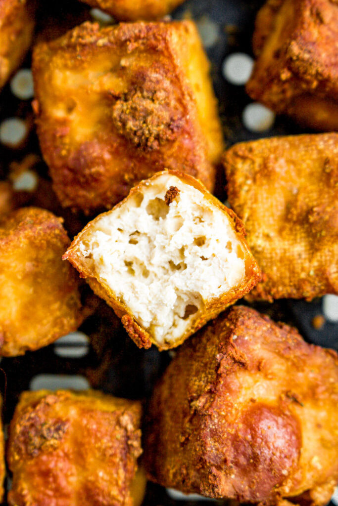 Overhead close up photo of a pile of crispy tofu cubes. The top one has a bite taken out of it.