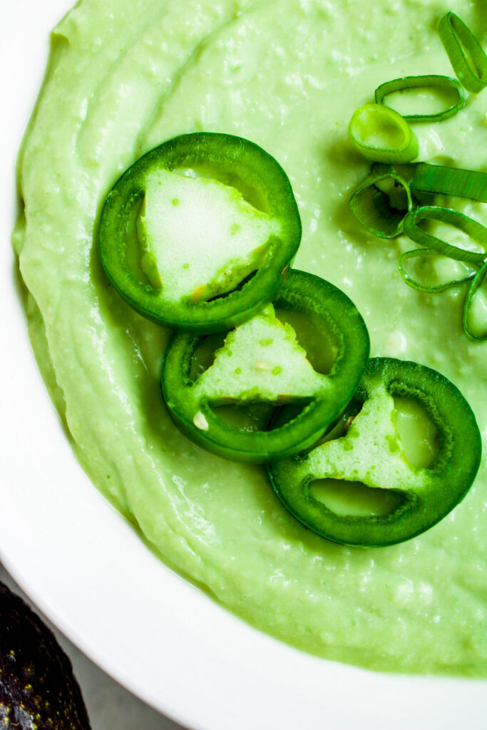 Overhead zoomed in photo of a bowl of Taco Bell avocado ranch sauce topped with sliced jalapenos and scallions