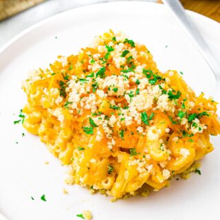 A square slice of vegan tofu mac and cheese on a plate sprinkled with minced herbs