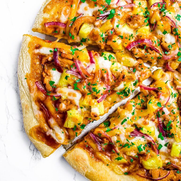 Overhead close up view of a slice of cheesy vegan BBQ chicken pizza with pineapple, herbs, and red onion