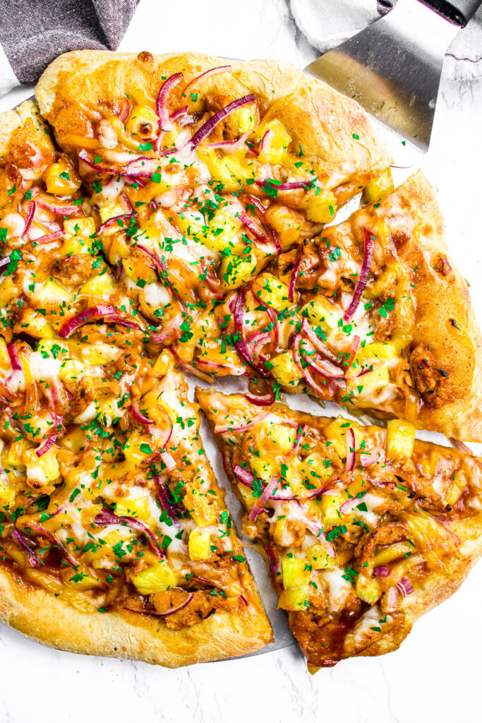 Overhead view of a sliced BBQ pineapple pizza with one slice to the bottom left pulled out