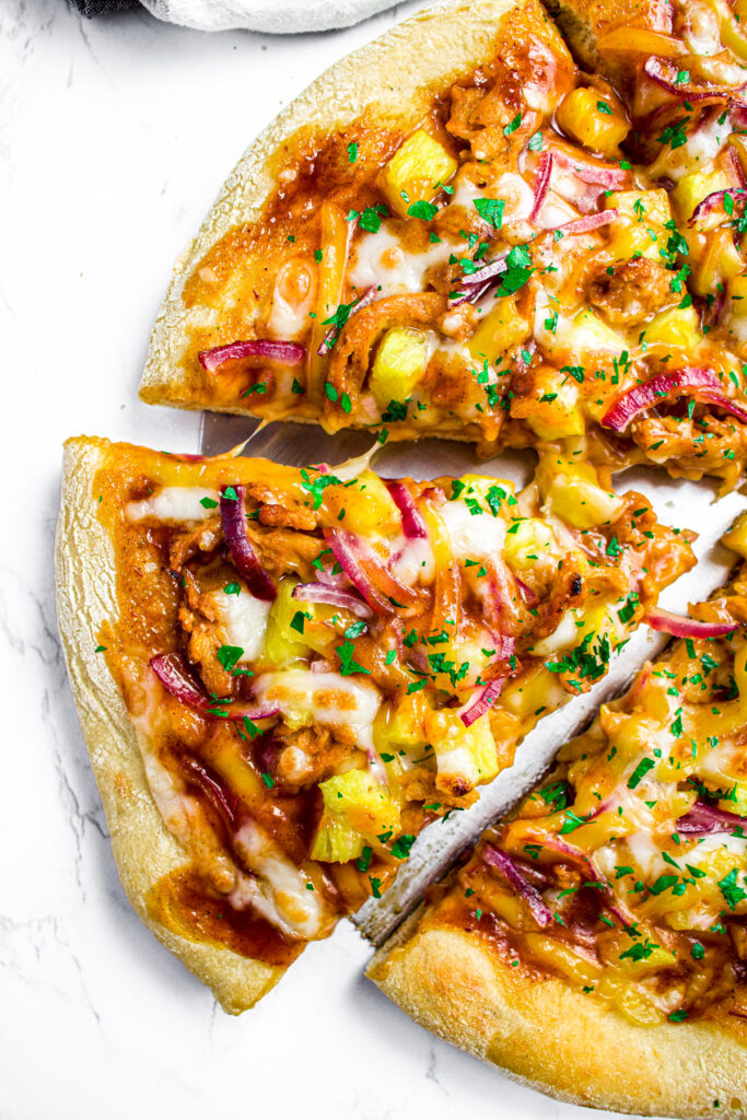 Overhead close up view of a slice of vegan BBQ chicken pizza with pineapple pulled out from the rest of the pie
