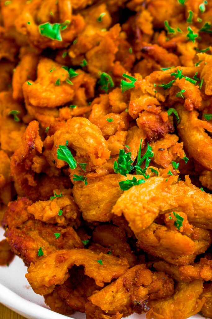 Close up shot of a pile of barbecue soy curls on a plate with minced fresh herbs on top