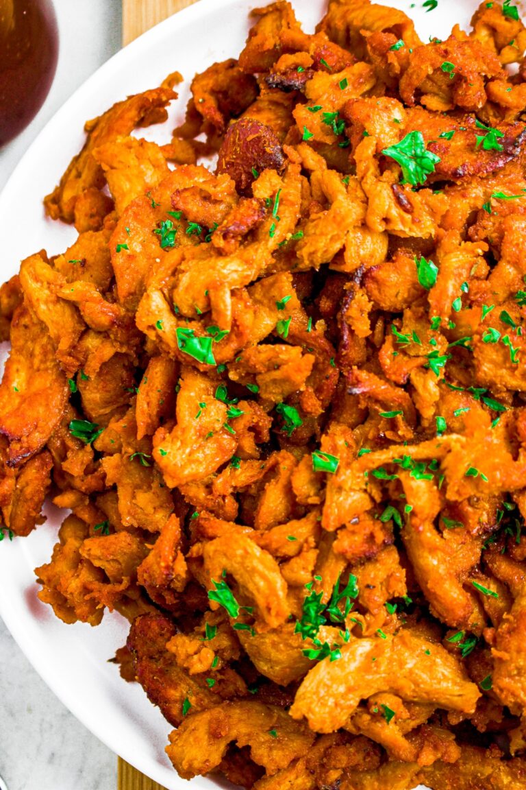 Overhead shot of half a round white plate with a pile of bbq soy curls on top sprinkled with fresh green herbs