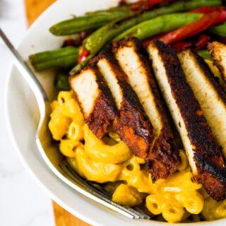Overhead close up photo of a round white bowl with mac and cheese, sliced bbq tofu, and seared green beans