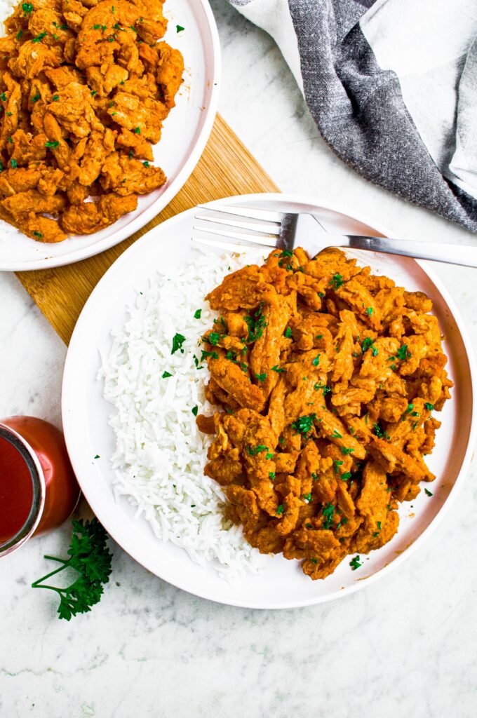 Overhead shot of two round white plates with vegan buffalo chicken and basmati rice sprinkled with fresh minced herbs