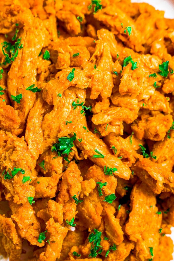 Zoomed in shot of a pile of vegan buffalo soy curl chicken sprinkled with minced fresh parsley