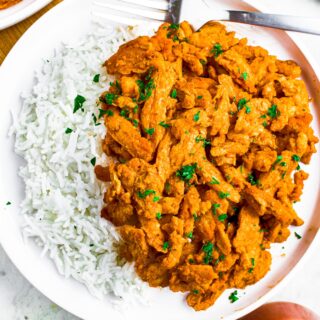 Overhead shot of a round white plate with white basmati rice on one side and buffalo soy curl chicken on the other. There is a clear glass jar of buffalo sauce in the bottom right corner.