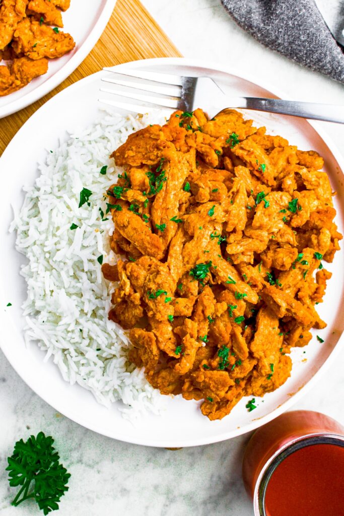 Overhead shot of a round white plate with white basmati rice on one side and buffalo soy curl chicken on the other. There is a clear glass jar of buffalo sauce in the bottom right corner.