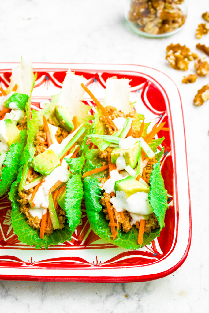 Overhead photo of half a plate of lettuce wraps with walnut meat, diced avocado, shredded carrot, and ranch drizzle