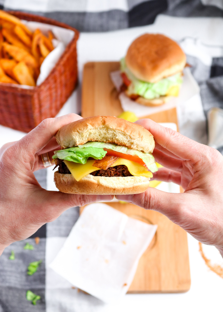 Overhead photo of two hands holding a vegan cheeseburger