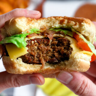 Close up photo of two hands holding a tvp burger with a big bite taken out of it.