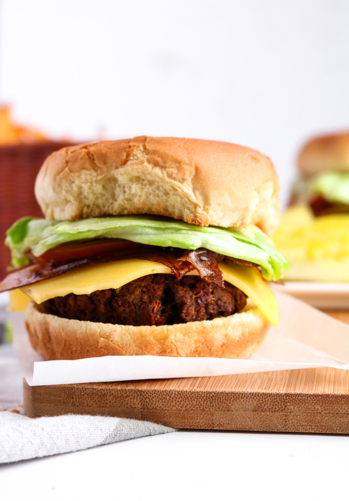 Head on photo of a homemade vegan burger with dairy free cheese, lettuce, and rice paper bacon