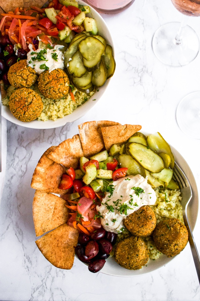 Overhead close up photo of two bowls of falafel salad with pickled onion, pita triangles, couscous, pickles, and tahini sauce