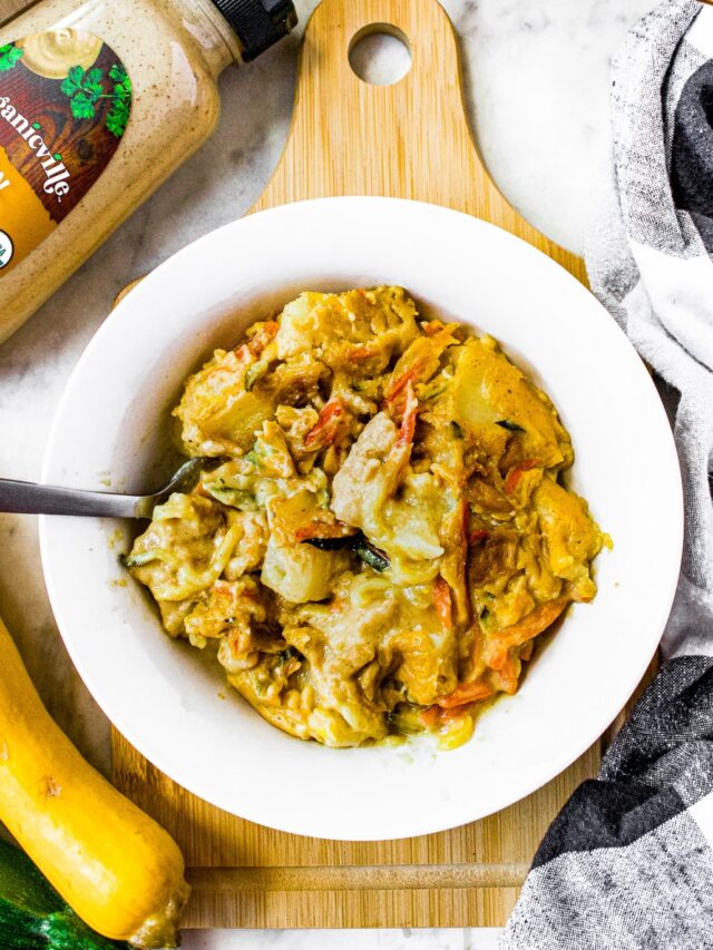 Overhead shot of a white bowl with dijon squash casserole in it surrounded by full squash and zucchini, a bottle of organicville dijon mustard, and a black and white linen