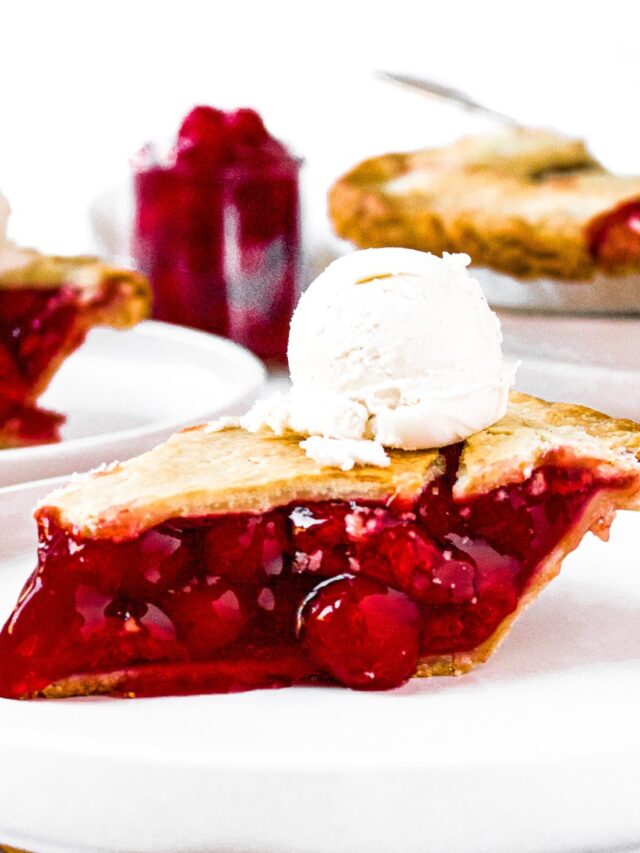 A head-on photo of a slice of cherry pie topped with a scoop of vanilla ice cream