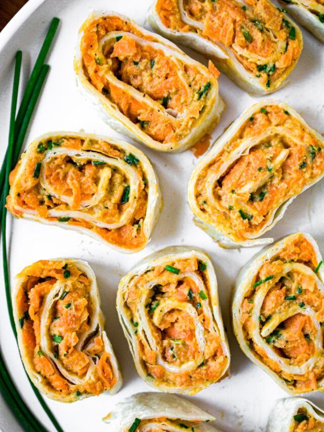 Close up overhead shot of 9 tortilla pinwheels on half a round plate with a fresh green onion off to the side.