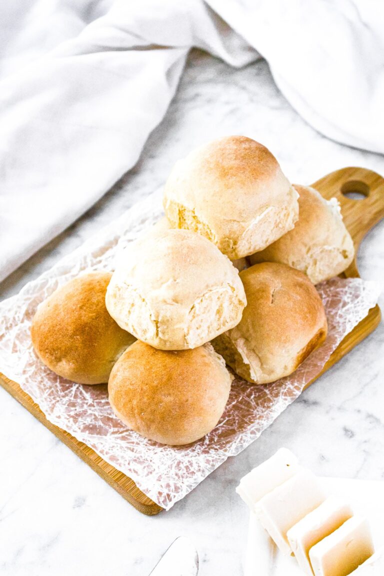 Overhead photo of a pile of 8 vegan dinner rolls on a rectangular wooden cutting board