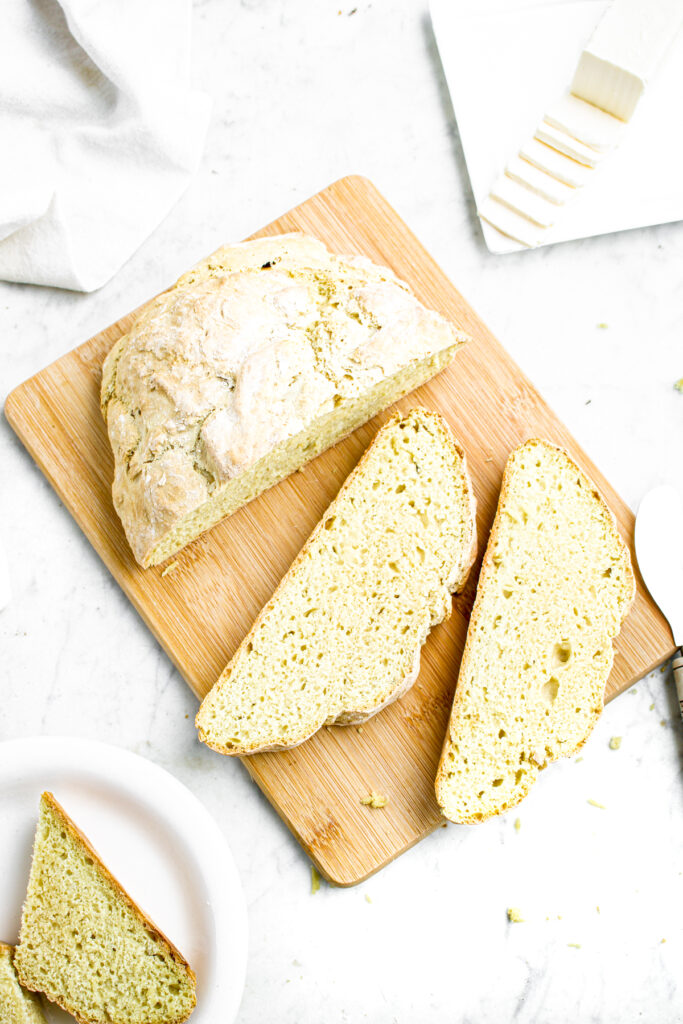 Overhead view of a round loaf of bread on a wooden cutting board partially sliced