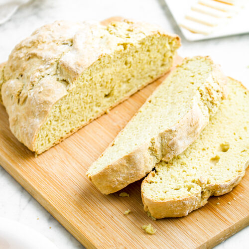 Overhead view of a half sliced loaf of vegan bread on a wooden cutting board in front of a stick of butter