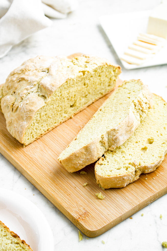Overhead view of a half sliced loaf of vegan bread on a wooden cutting board in front of a stick of butter