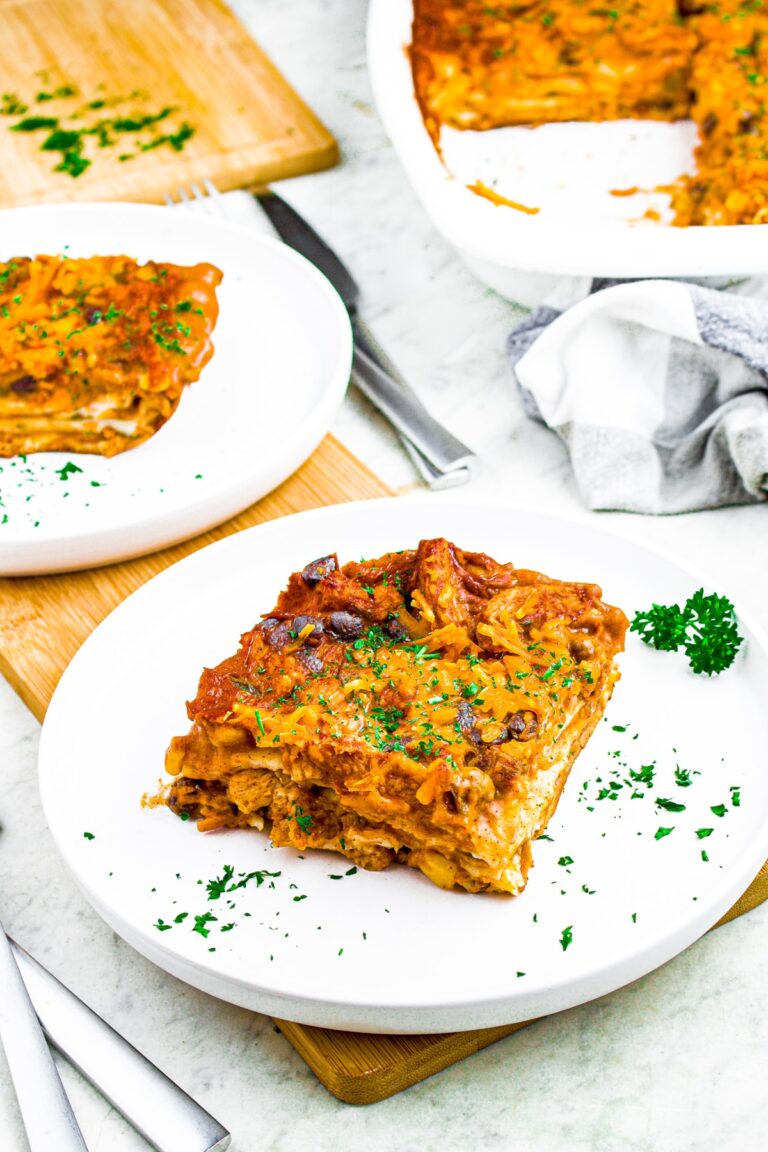 Overhead shot of two round plates with slices of enchilada casserole on them sprinkled with green herbs