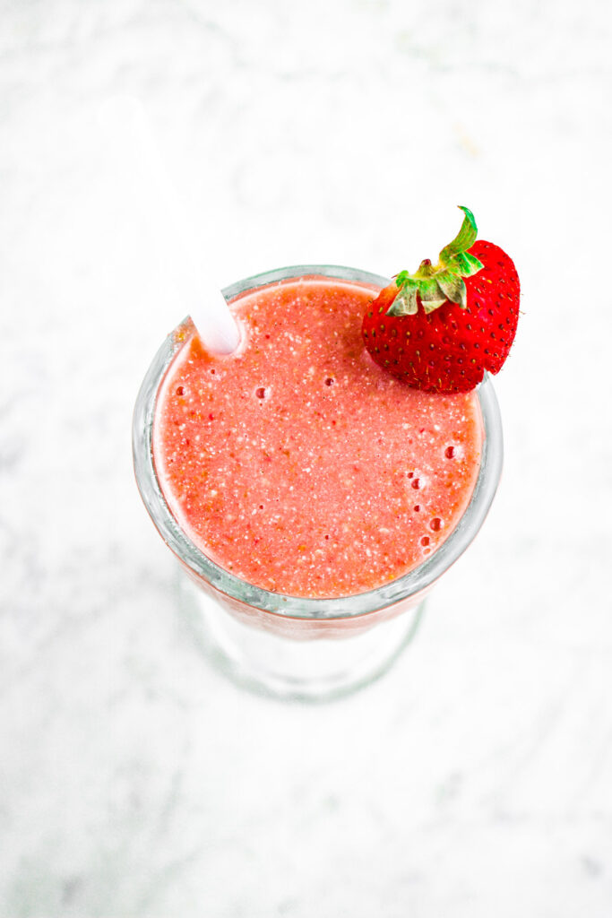 Overhead photo of a cherry smoothie in a glass with a straw and strawberry on the rim