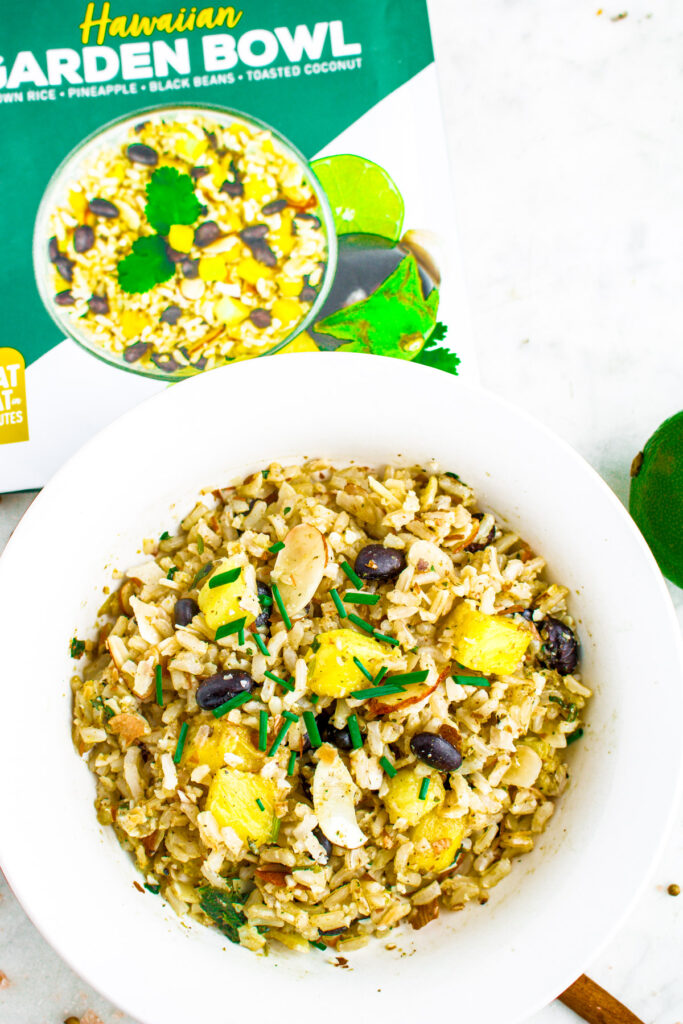 Overhead photo of a round white bowl with rice, pineapple, and black beans next to a Frozen Garden garden bowl packet