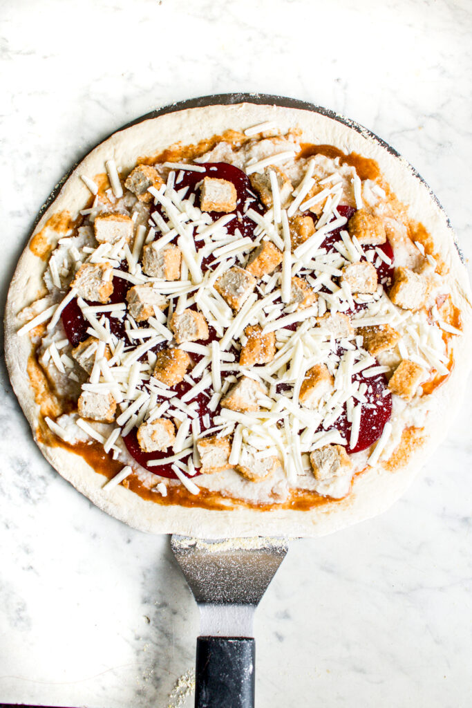Overhead view of an assembled pizza on a pizza peel before baking