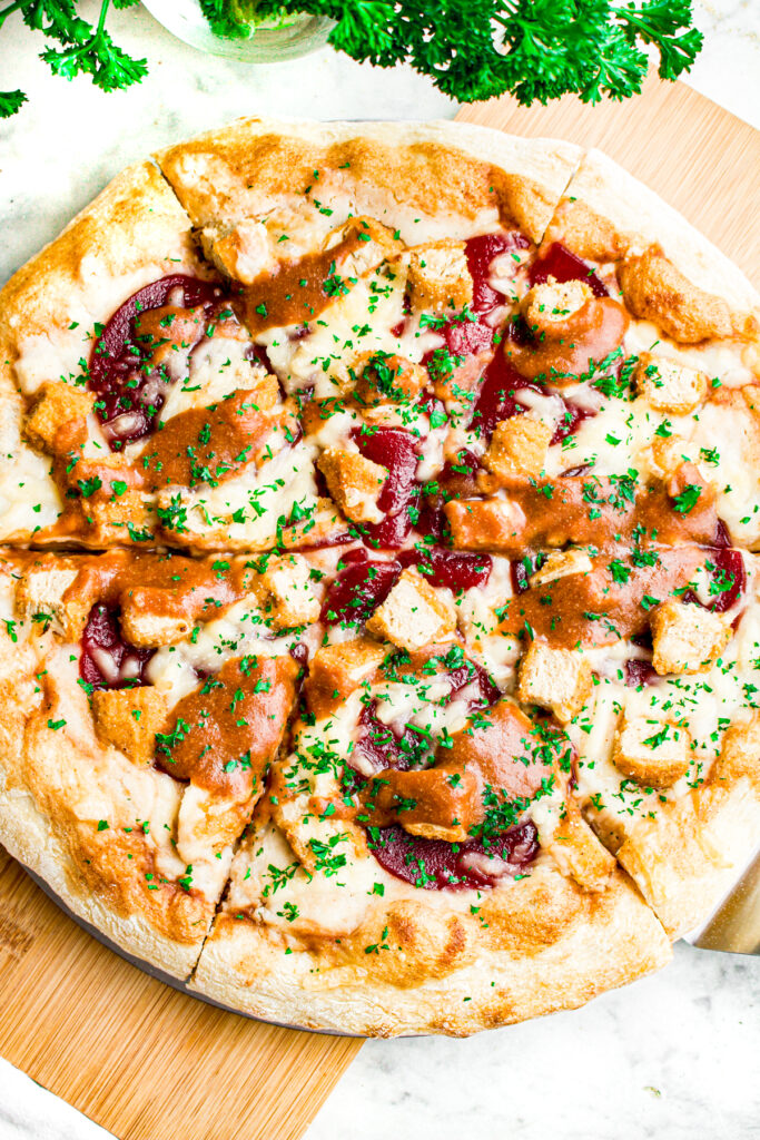 Overhead view of a sliced vegan Thanksgiving leftover pizza with mashed potatoes, cranberry sauce, seitan, and gravy
