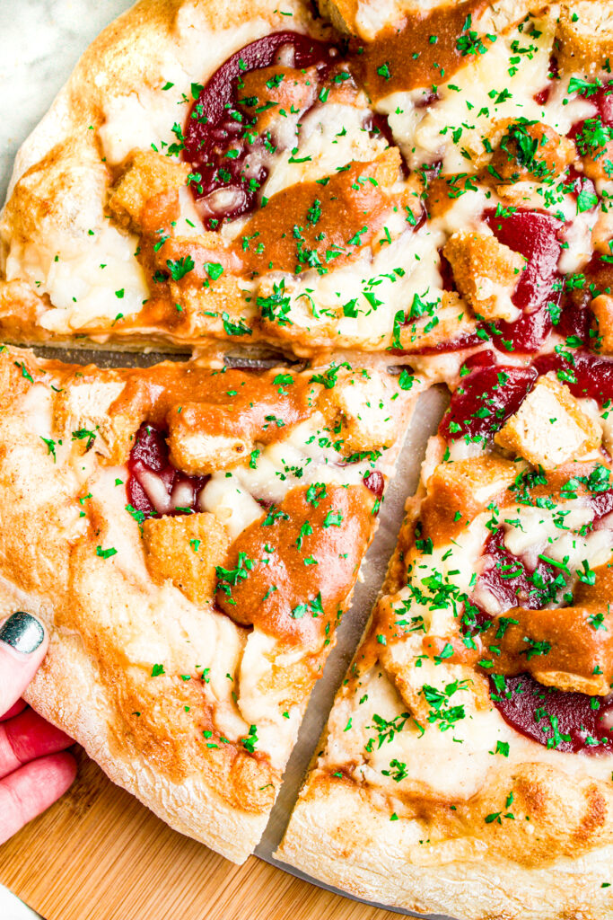 Close up overhead view of a hand pulling a slice of vegan thanksgiving pizza out of a full pie