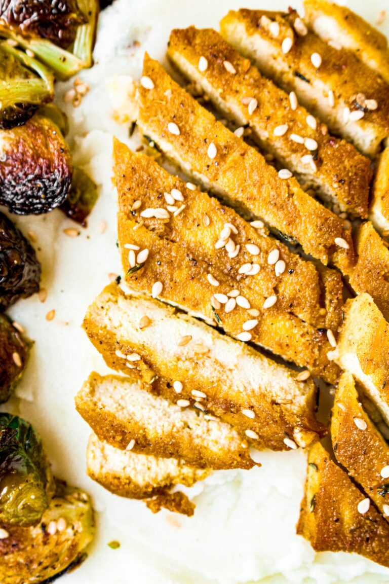 Overhead close up shot of a sliced baked tofu cutlet, with some pieces falling down the side of the mashed potato mountain