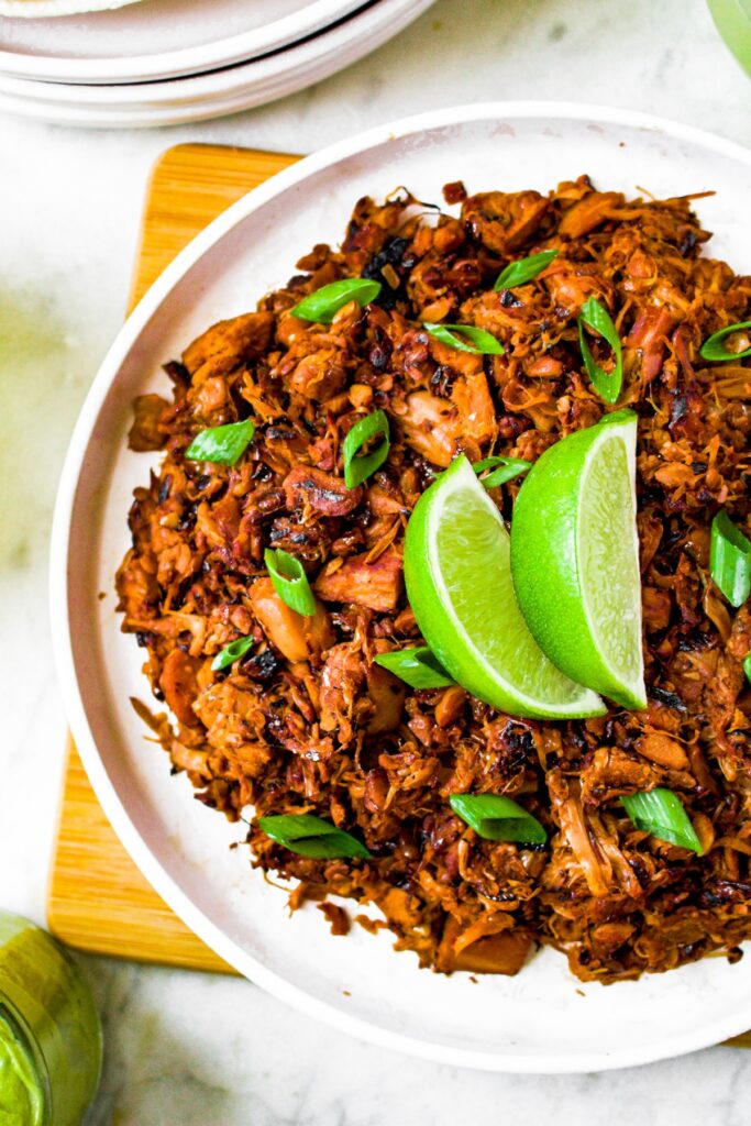 Overhead photo of a plate of jackfruit carnitas garnished with two lime slices and fresh herbs.