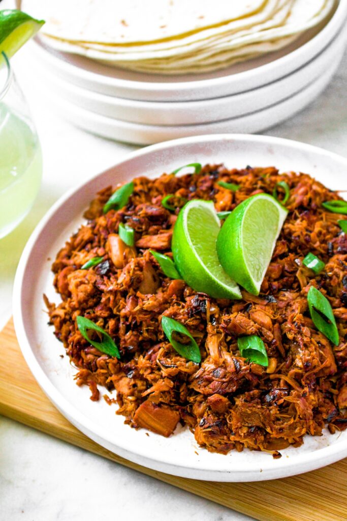 Overhead photo of a plate of vegetarian carnitas topped with lime wedges and sliced scallions