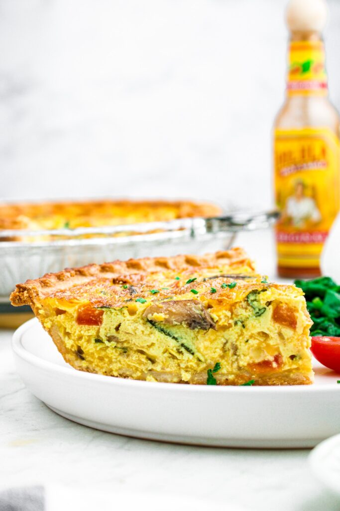 Head on close up photo of a slice of vegan quiche with a hot sauce bottle in the background
