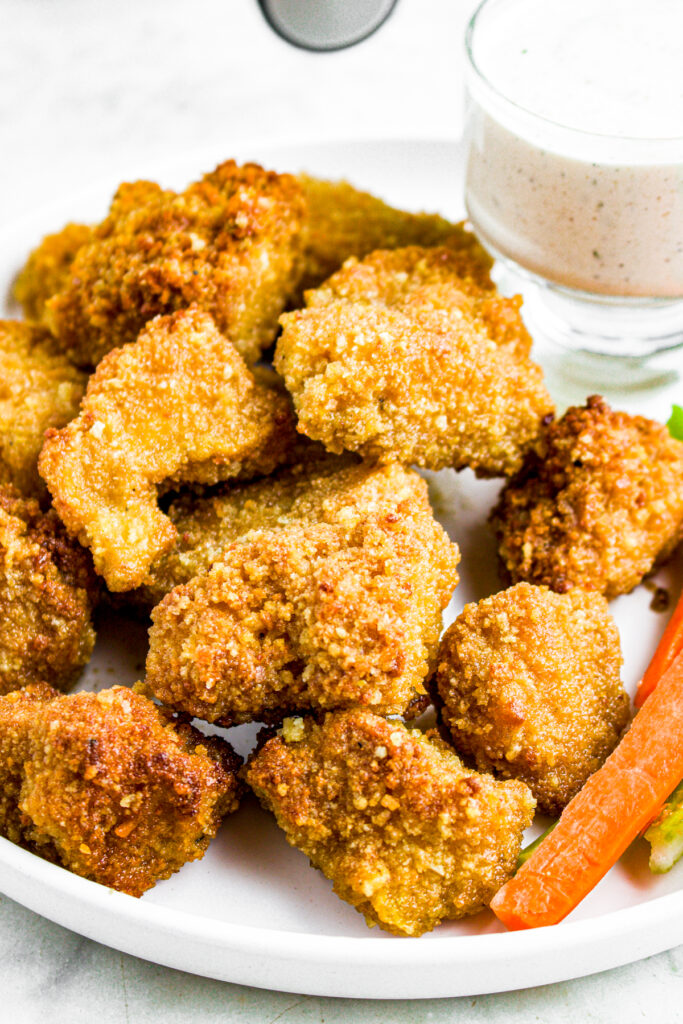 Overhead close up view of breaded tofu wings on a round white plate next to carrot sticks and celery sticks