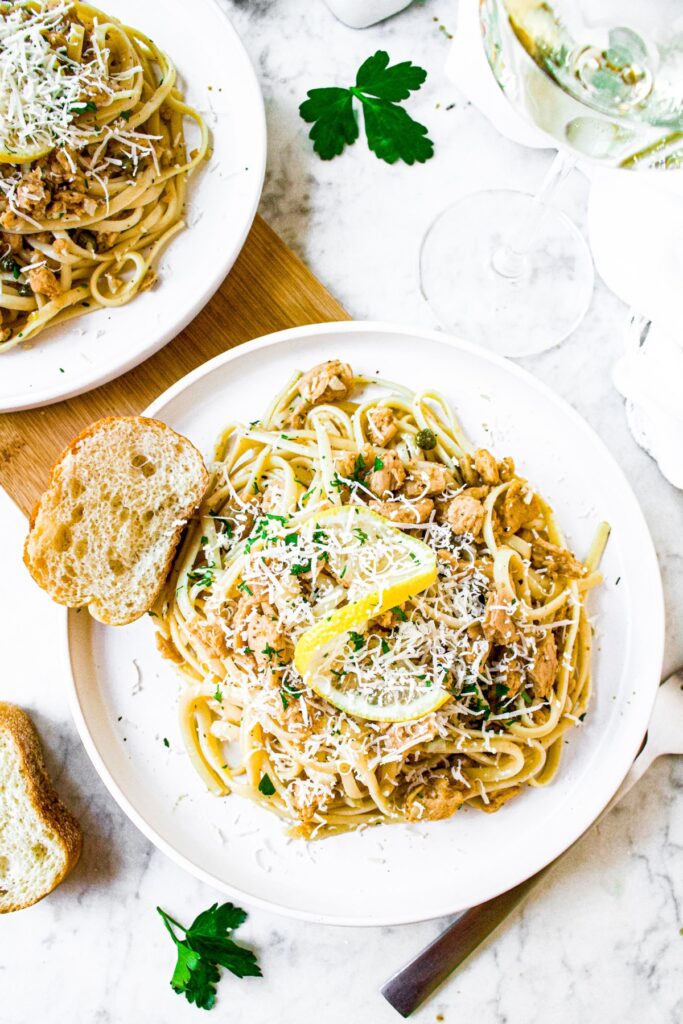 Overhead shot of a plate of vegan linguine clam sauce topped with fresh green herbs, vegan parmesan, and a twisted lemon rind