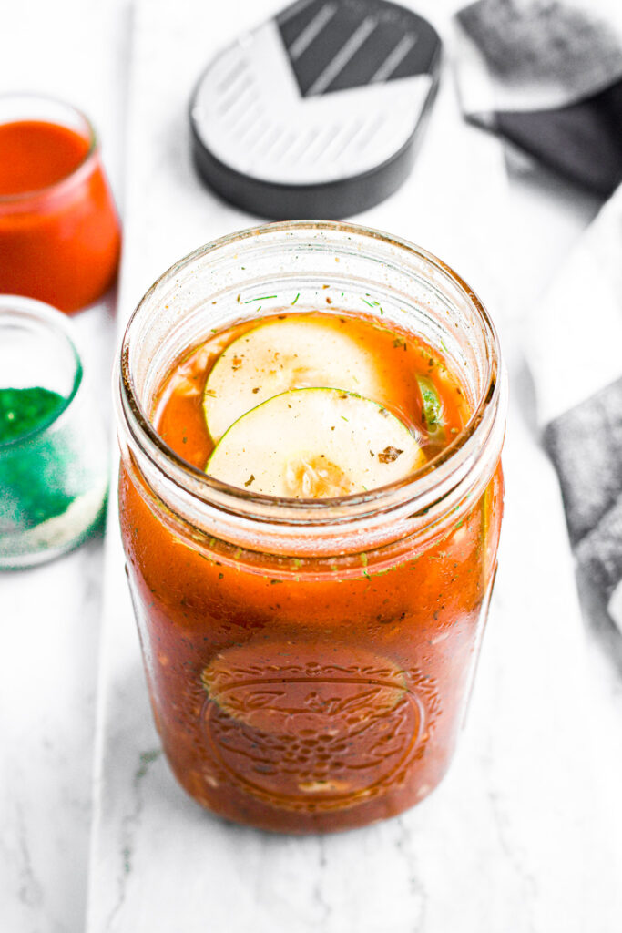Overhead view of fresh buffalo ranch refrigerator pickles in a large clear mason jar with a jar of buffalo sauce behind it