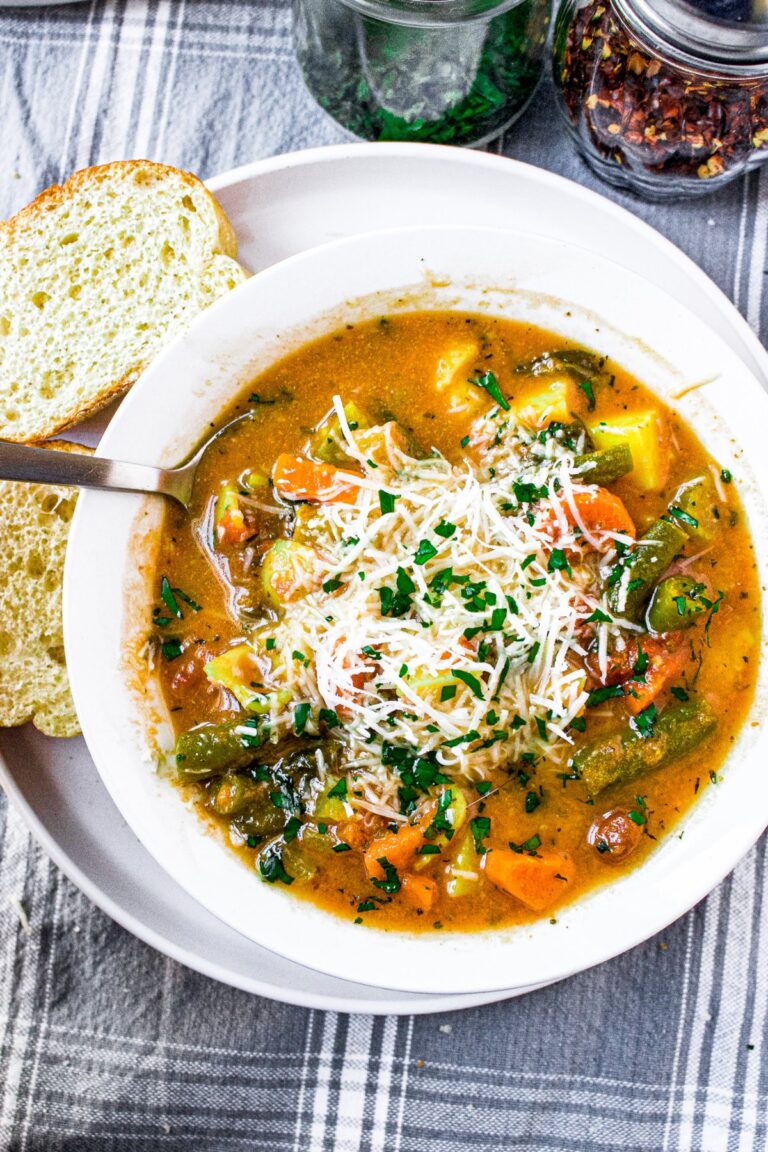 Overhead photo of a round white bowl of minestrone soup topped with grated dairy-free parmesan