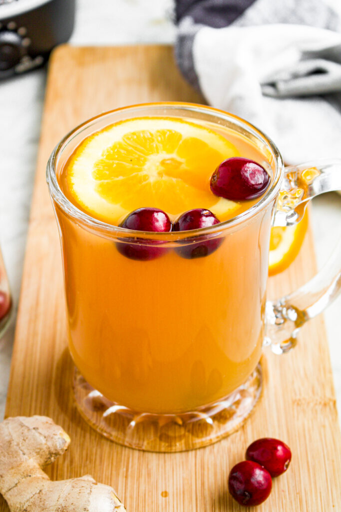 Close up overhead view of a clear glass mug of spiced cider with cranberries, an orange slice, and a cinnamon stick floating on top