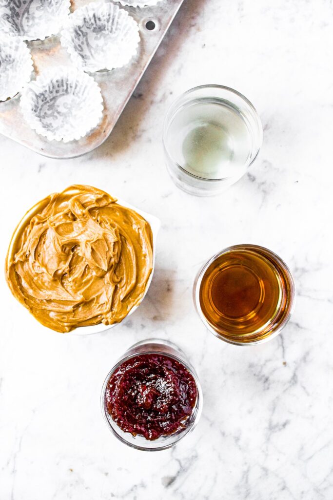 Overhead shot of all the ingredients you need to make pbj cups: creamy peanut butter, maple syrup, coconut oil, strawberry jam
