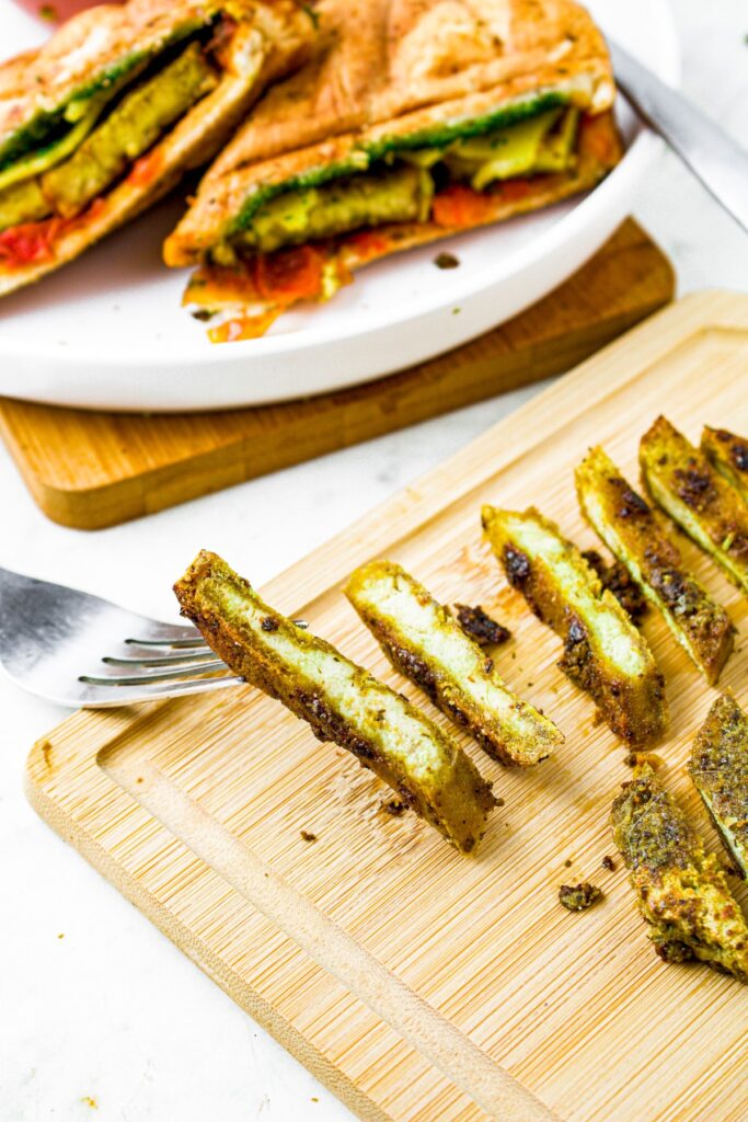 Overhead shot of a fork lifting up a piece of vegan pesto tofu on a cutting board