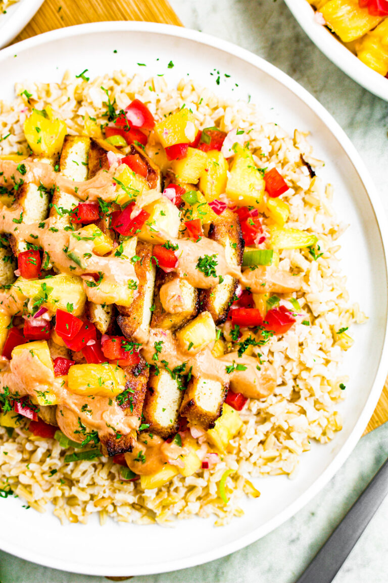 Overhead zoomed in photo of a plate of brown rice with teriyaki tofu, pineapple salsa, and drizzled with vegan spicy mayo