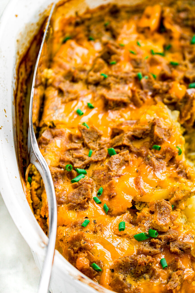 Zoomed in photo of a cheesy casserole in a white ceramic baking dish with a spatula sticking into the side