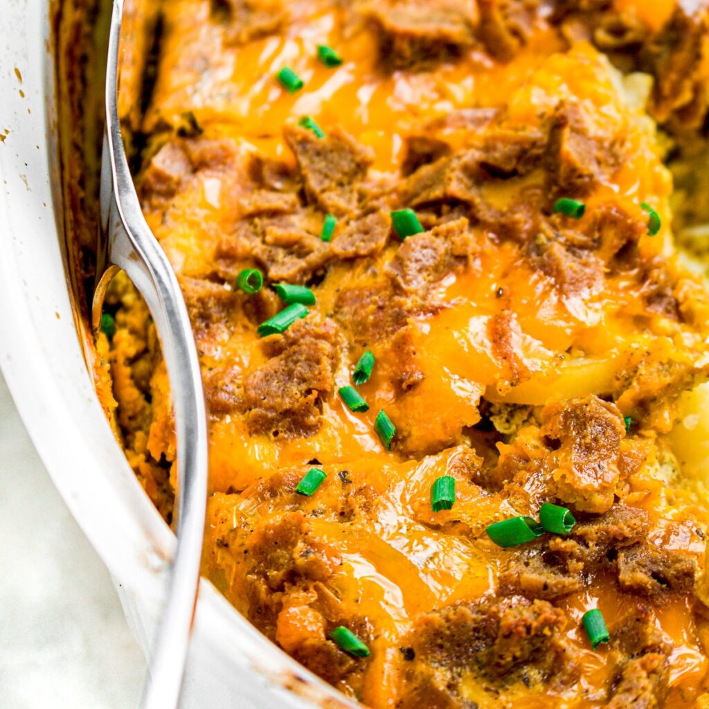 Zoomed in photo of a cheesy casserole in a white ceramic baking dish with a spatula sticking into the side